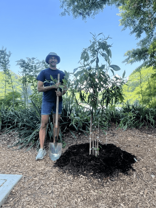 Ashley stands beside a newly planted commemorative Sweetbay Magnolia tree in Piedmont Park overlooking Lake Clara Meer.